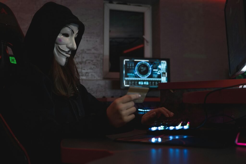 Contact Us 1 Masked hacker with credit card at computer, symbolizing cybercrime and anonymity.